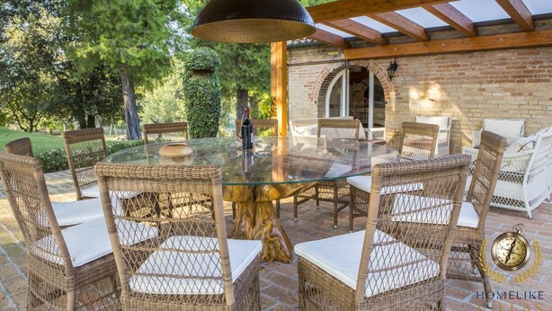 An outdoor dining area with wicker chairs and a glass table, surrounded by brick walls and greenery. - Villa Panperduto (Potenza Picena)