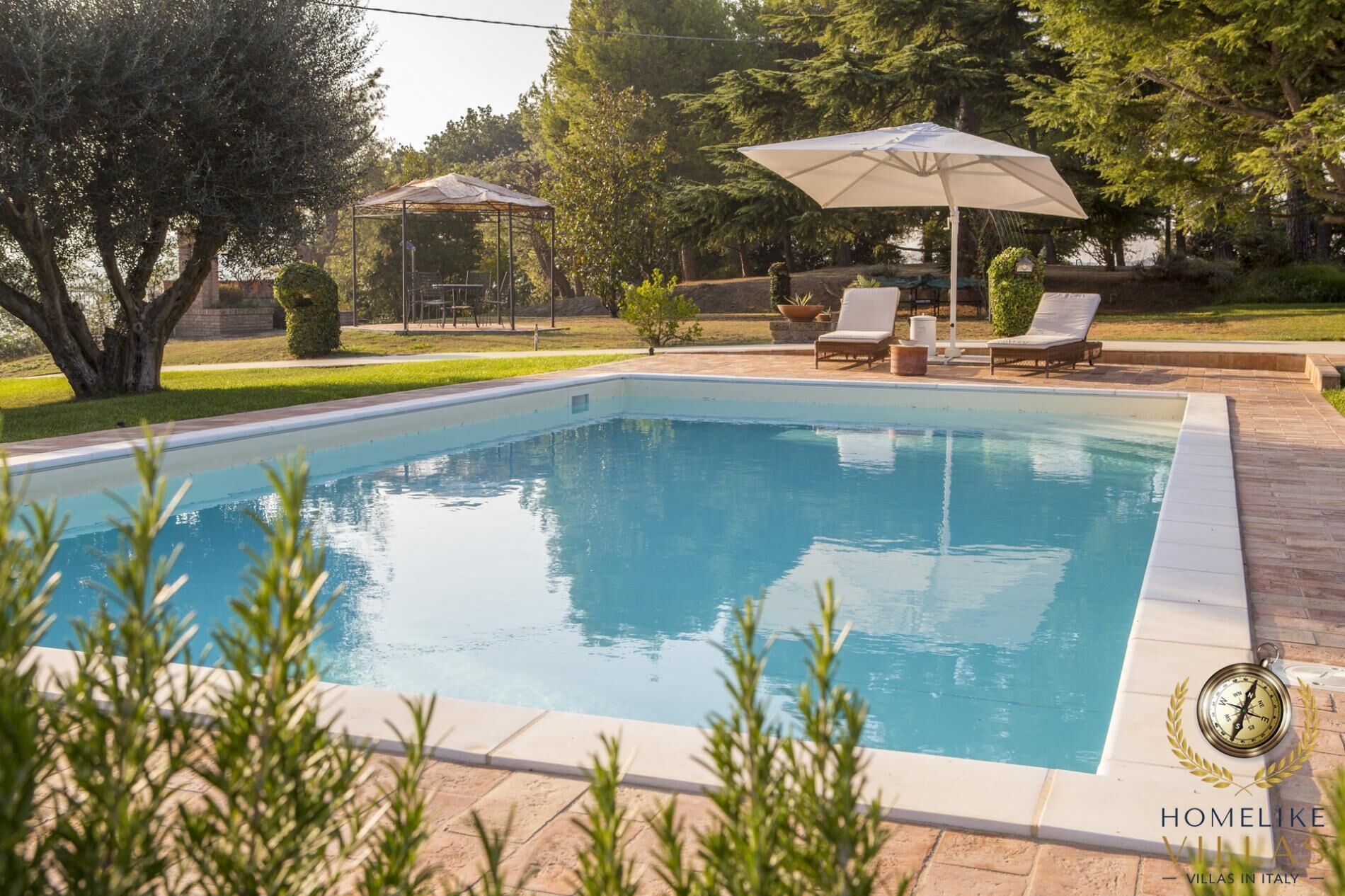 Piscina com borda em azulejo, rodeada por um espaço de estar com espreguiçadeiras e uma pérgola.