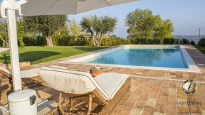 A swimming pool with a white umbrella, wicker furniture, and a view of trees and hills. - Villa Panperduto (Potenza Picena)