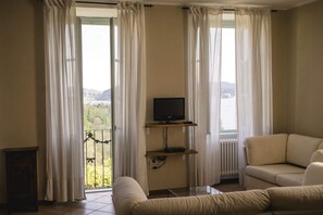 A living room with a sofa, a television on a stand, and a view of a lake through large windows with sheer curtains.