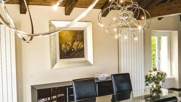 Zona pranzo con tavolo in vetro, sedie nere, un lampadario e un quadro appeso al muro.