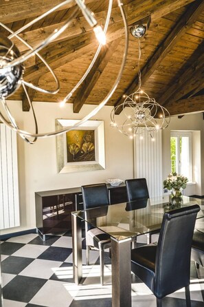 A dining area with a glass table, black chairs, a chandelier, and a painting on the wall.