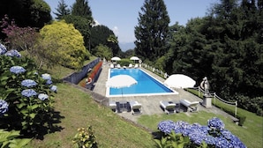 Piscina rectangular con borde de piedra, rodeada de sillas de descanso y sombrillas.