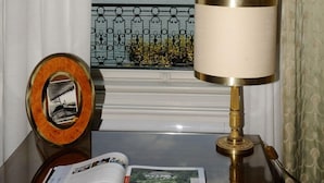 Una habitación con vistas a un lago y montañas, una lámpara, un libro y un espejo decorativo sobre una mesa de madera.