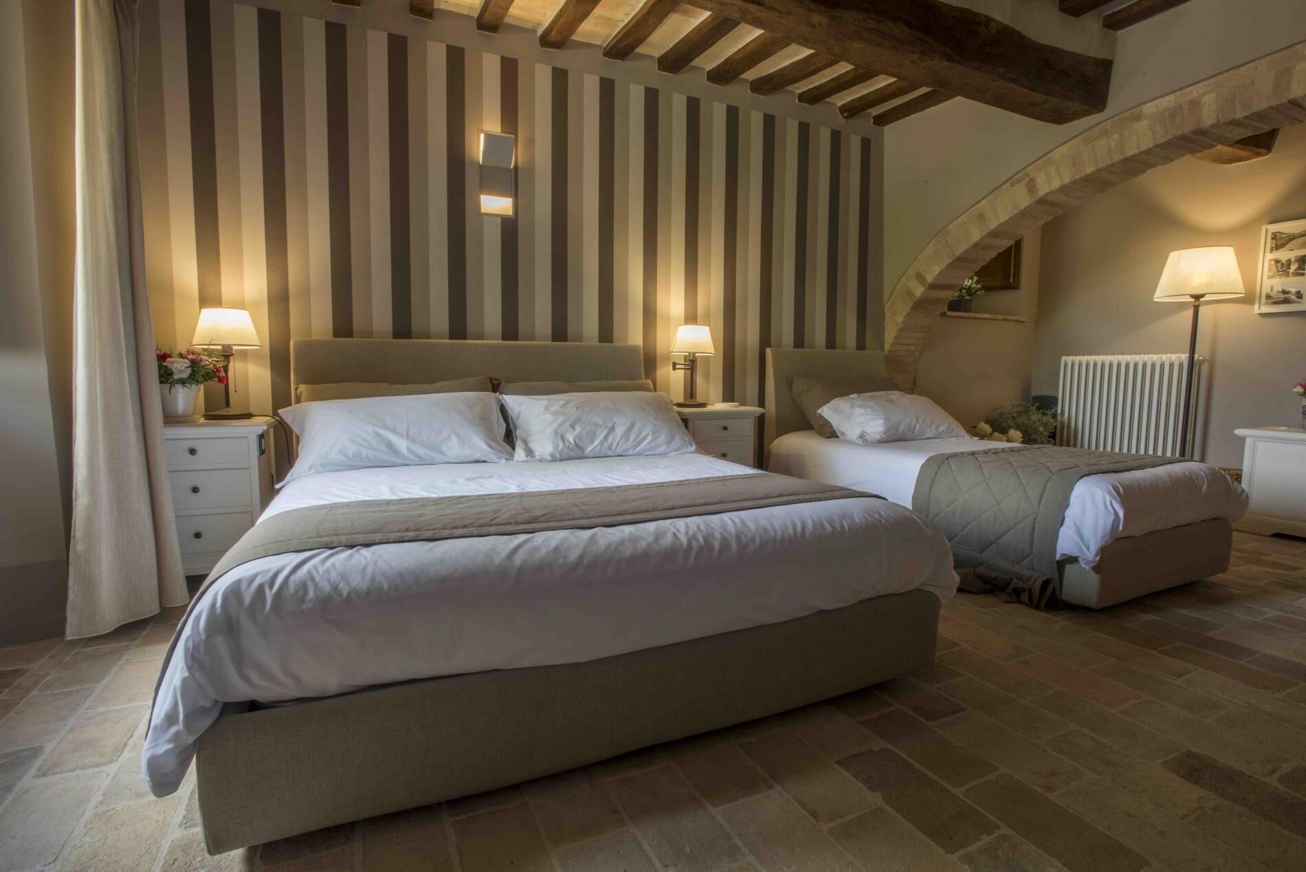 A bedroom with two beds, striped wallpaper, and a stone floor.