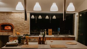 Una cocina moderna con una isla central, iluminación colgante y un horno de ladrillo.