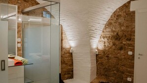 Un baño moderno con cabina de ducha de vidrio, pared de piedra y alfombra redonda con un libro.