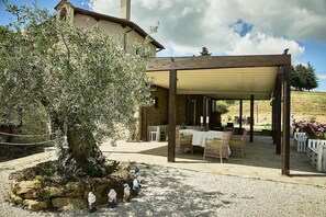 A covered outdoor seating area with tables and chairs, a stone wall, and a large tree. - Villa Panorama (Monte Santa Maria Tiberina)