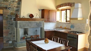 Una cocina rústica con chimenea de piedra, armarios de madera y un comedor con una mesa preparada para dos.