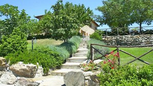 Una escalera de piedra conduce a una casa de piedra rústica rodeada de abundante vegetación y un muro de piedra.