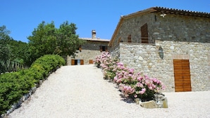 Un edificio de piedra con camino de grava y flores rosadas.