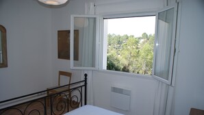 Une chambre à coucher avec un lit, une fenêtre donnant sur un paysage dégagé, une chaise et un radiateur.