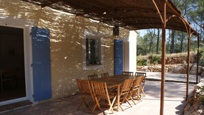 Une terrasse extérieure avec une table et des chaises en bois, un espace couvert et un mur en pierre.