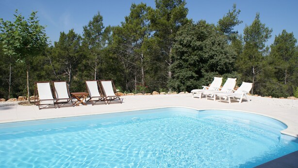 Une piscine bordée de chaises longues blanches, avec un ciel bleu clair en arrière-plan.