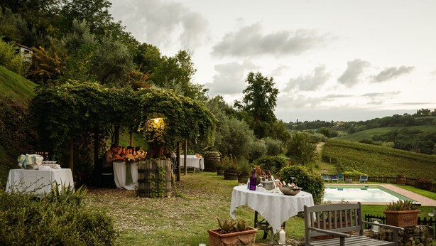 An outdoor dining area with tables and chairs, a stone wall, and a pool in the background. - Fienile (4+2) beautiful apartment with pool in Chianti between Florence and Siena (Tavarnelle Val di Pesa)