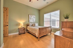 Un dormitorio con cama de madera, mesita de noche, lámpara, ventana con persianas y puerta.