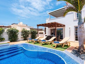 Un área de piscina en la azotea con sillones y una pérgola.