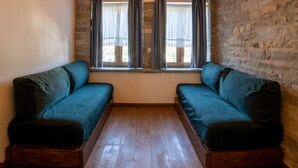 Una habitación con techo inclinado, vigas de madera, pared de piedra y una ventana con cortinas.