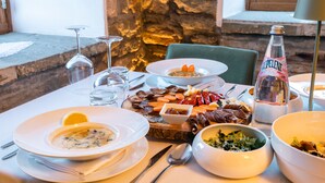 Una mesa de comedor dispuesta con varios platos, entre ellos sopa, ensalada y carnes, con una botella de agua y vasos sobre la mesa.