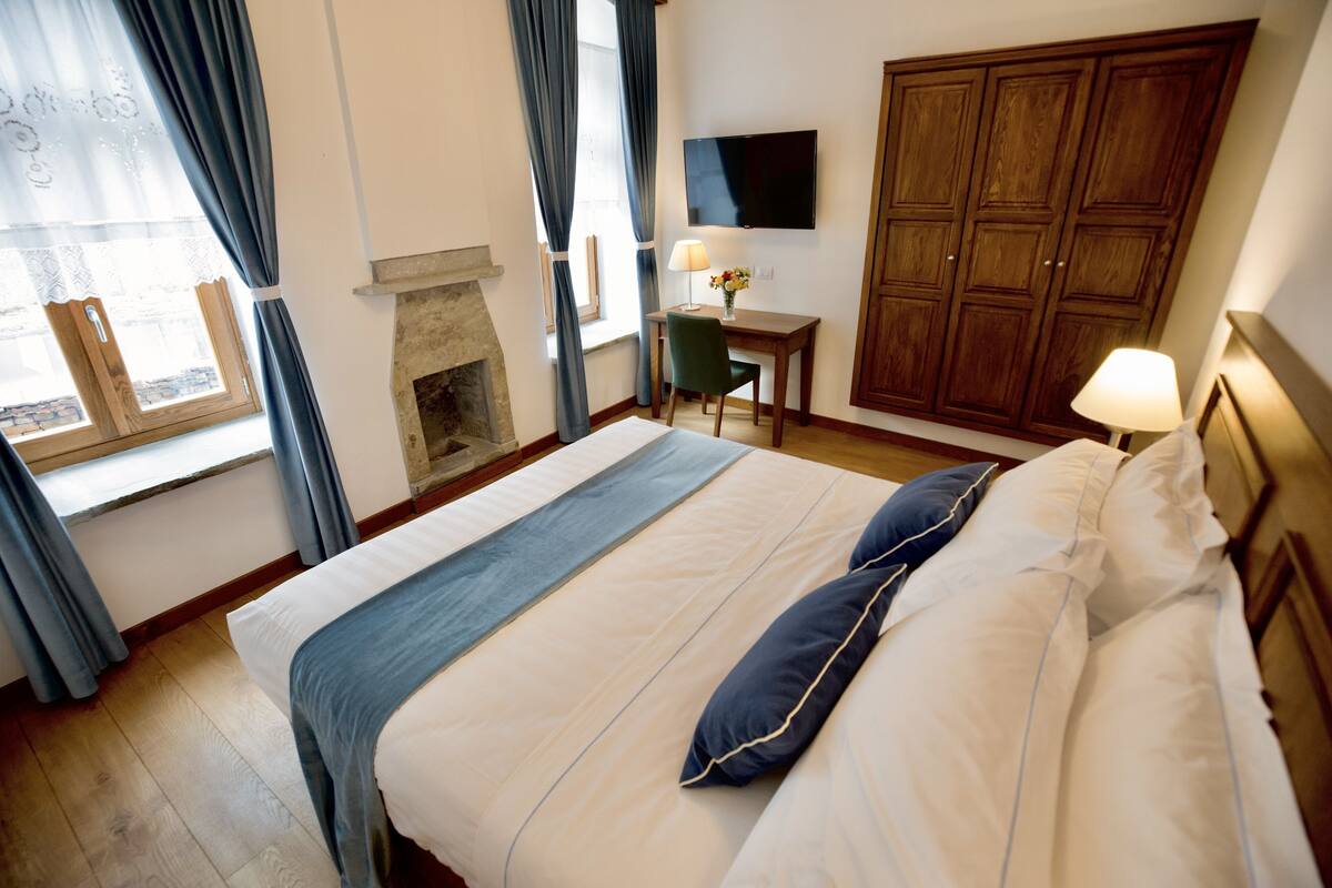Una habitación de hotel con una cama grande, un escritorio con silla, un televisor y un armario.