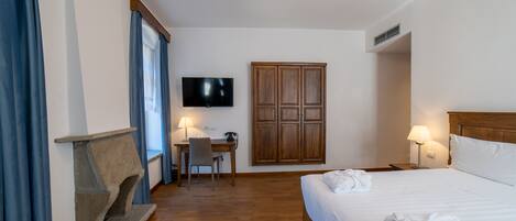 A hotel room with a bed, a desk with a chair, a television, a wardrobe, and a stone fireplace.