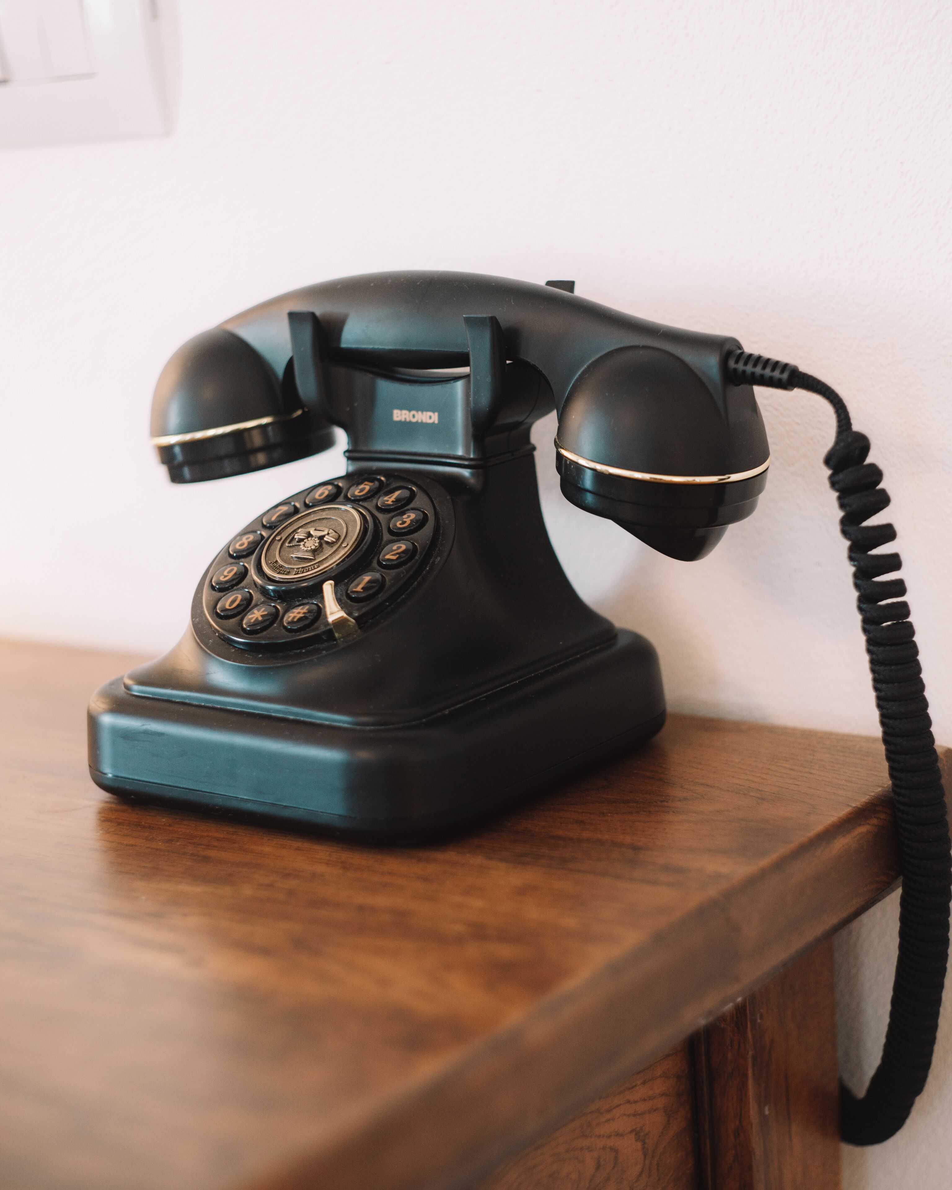Un vieux téléphone noir posé sur une table en bois, devant un mur blanc.