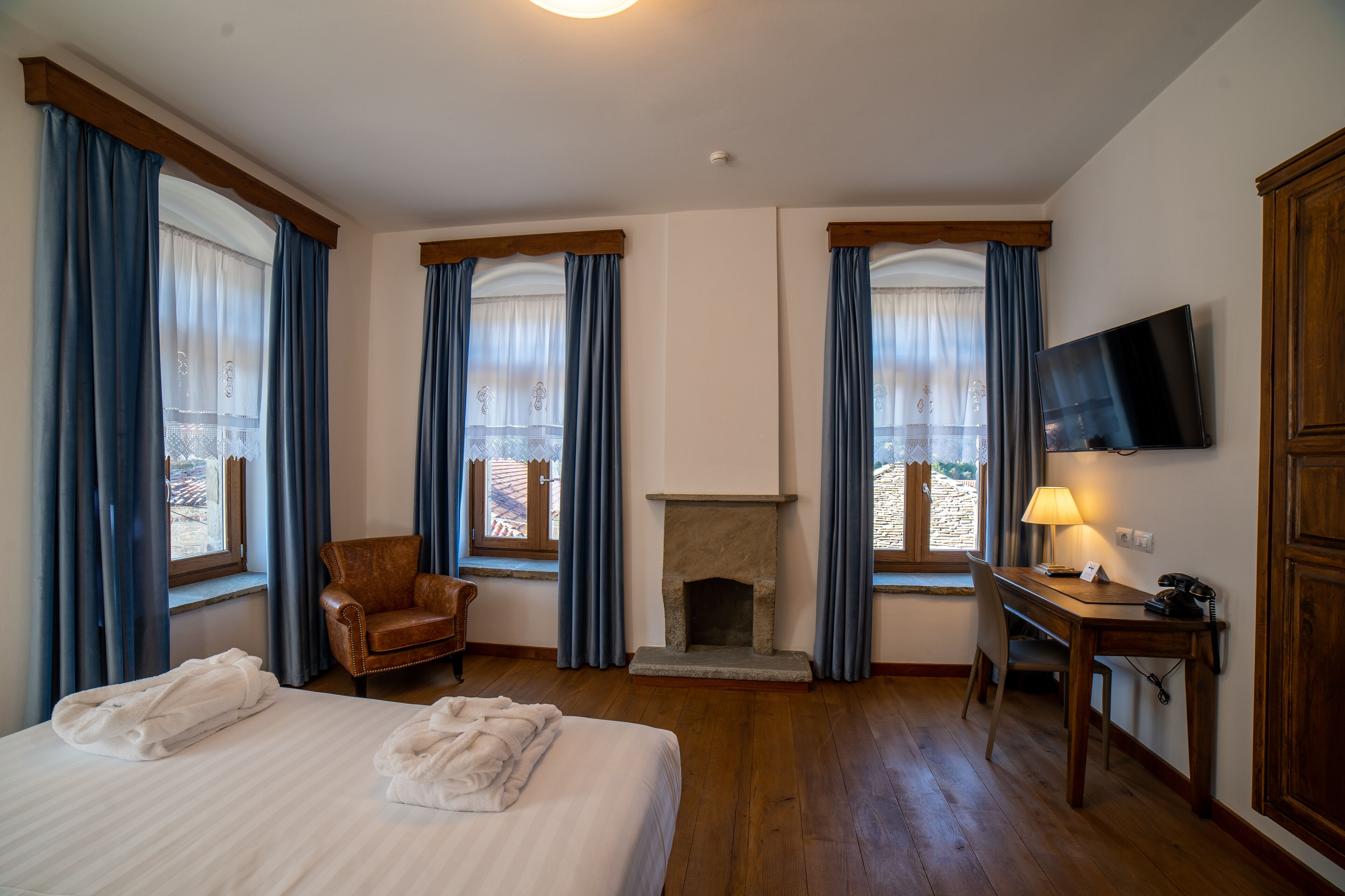 A hotel room with a bed, a chair, a desk, a fireplace, and a TV mounted on the wall.