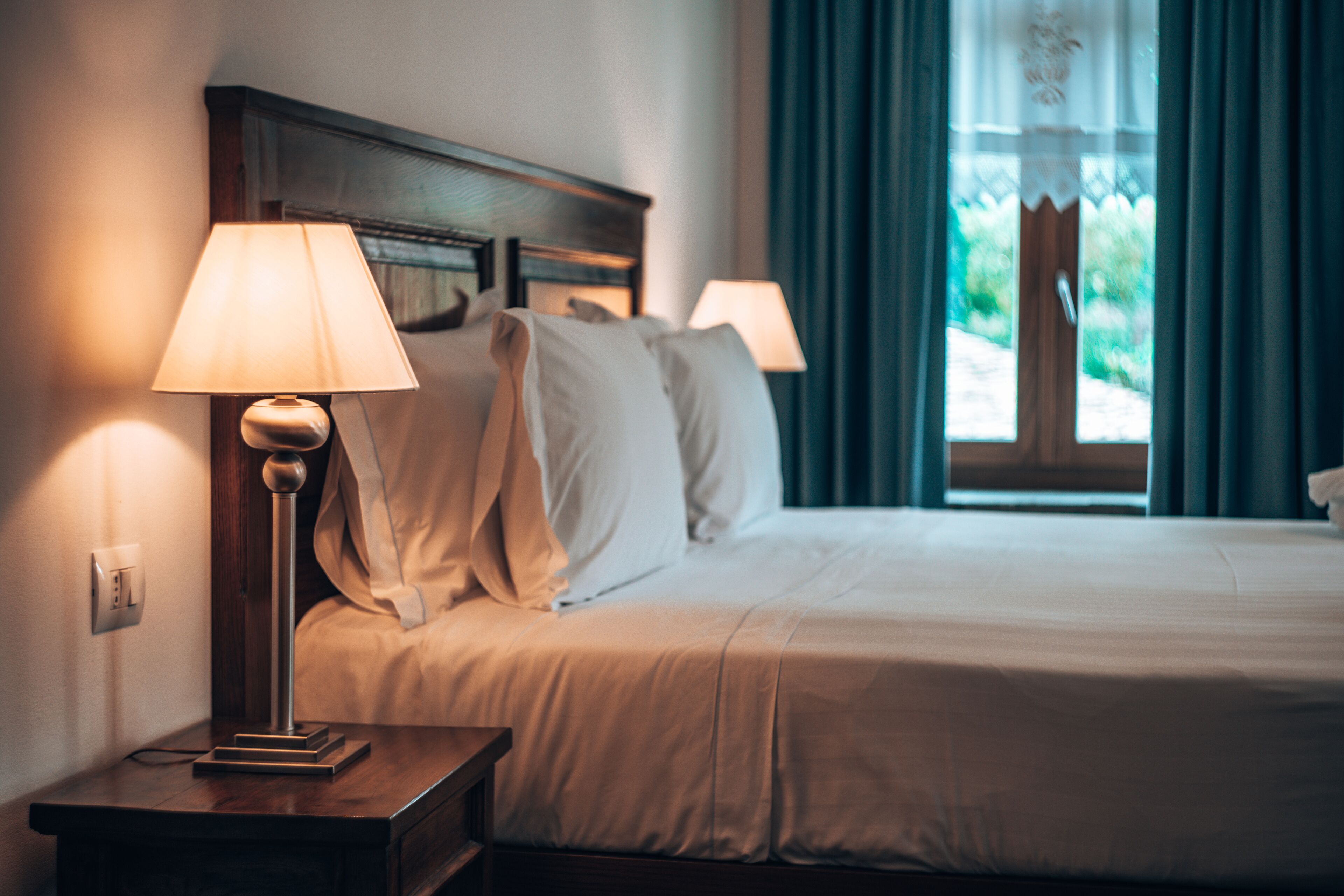 Una cama bien hecha con sábanas blancas, un cabecero de madera y dos lámparas de noche.