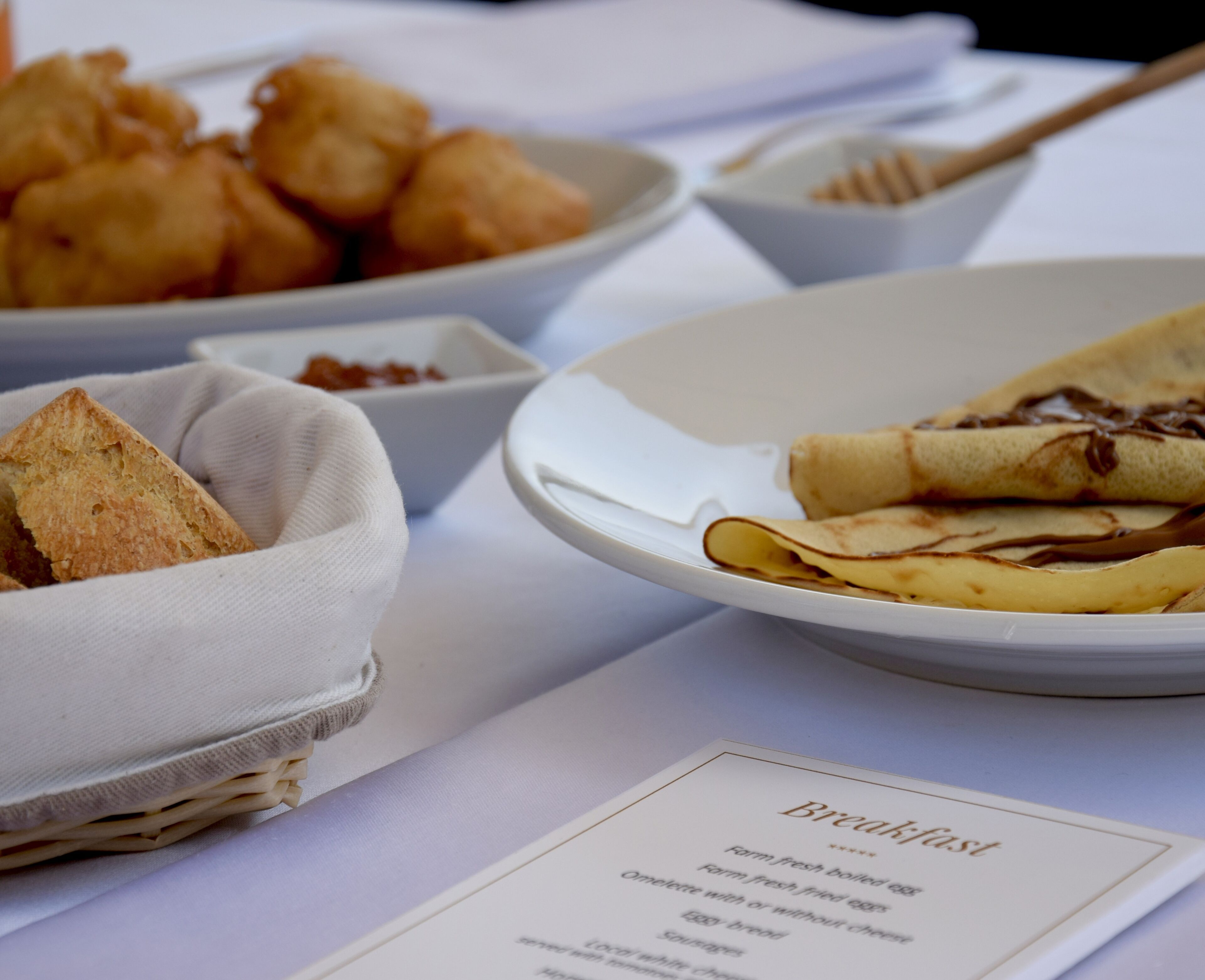 Ein Frühstücksbuffet mit Speisekarte, Pfannkuchen mit Sirup, einem Korb mit Croissants und einer Obstschale.