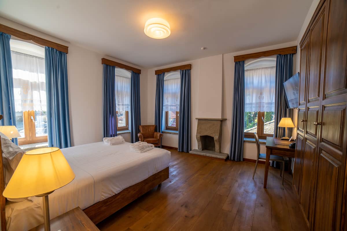 Una habitación de hotel con una cama grande, un escritorio de madera, una silla, chimenea y televisor sobre un mueble.
