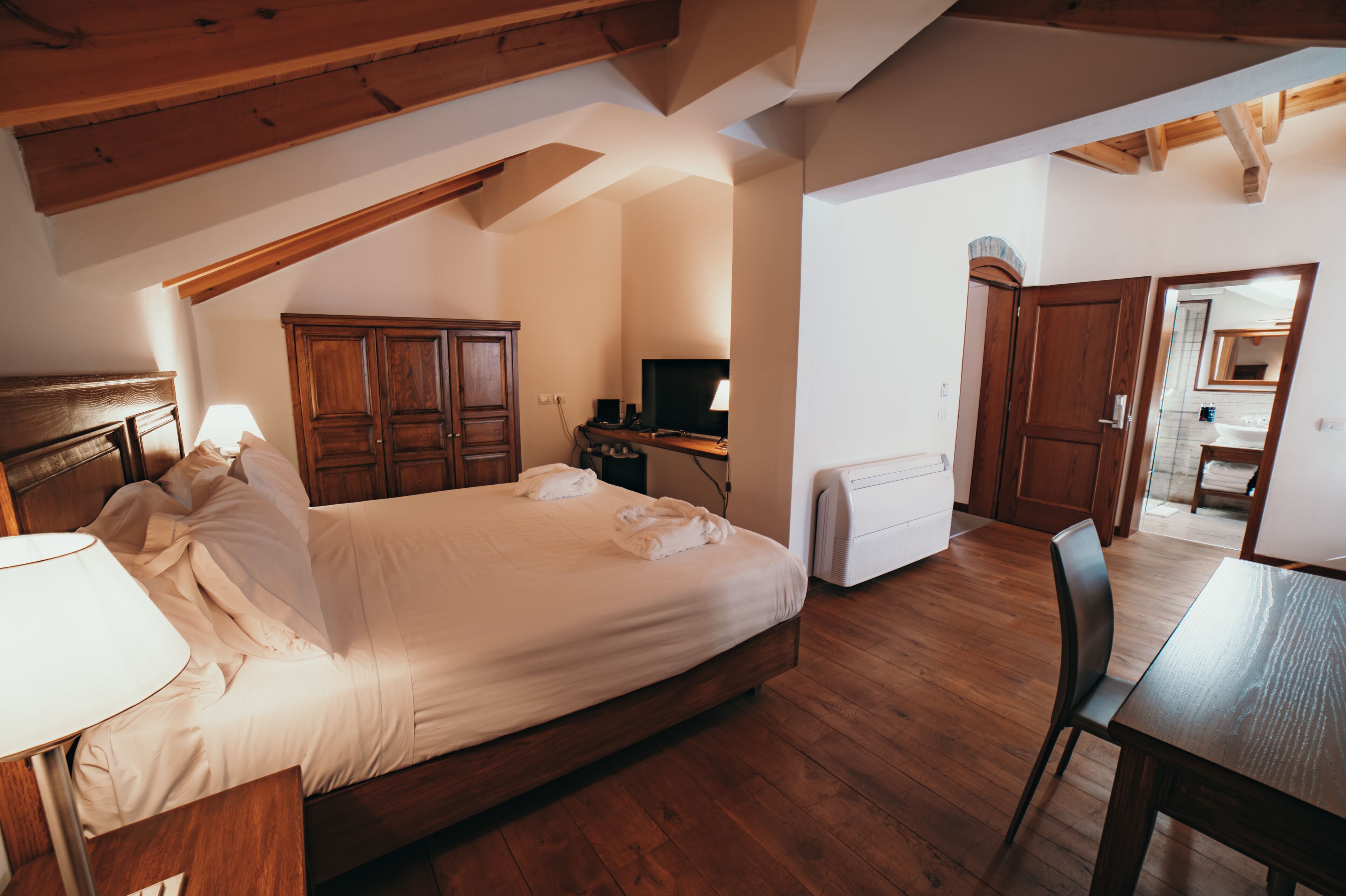Un dormitorio con una cama de madera, un escritorio, una silla, un televisor y una zona de cocina.