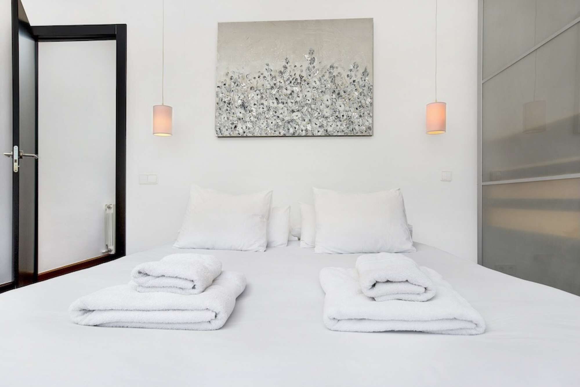 Ein Hotelzimmer mit einem Bett, zwei Kissen, einem gefalteten Handtuch, einem Gemälde und zwei Wandleuchten.