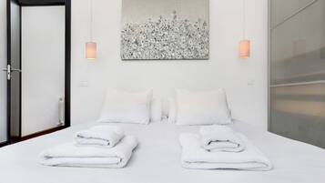 Ein Hotelzimmer mit einem Bett, zwei Kissen, einem gefalteten Handtuch, einem Gemälde und zwei Wandleuchten.