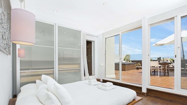 A bedroom with a large bed, a sliding glass door leading to an outdoor patio, and a ceiling light fixture. - Spectacular penthouse with terrace (Barcelona)