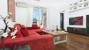A modern living room with a red sofa, a coffee table, and a TV on the wall. - Spectacular penthouse with terrace (Barcelona)