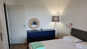 A bedroom with a bed, a dresser, a mirror, a lamp, and a door. - Magnificent T2 parahotelier with 23m2 south-facing terrace and sea view (Ajaccio)