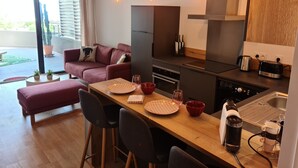 A modern kitchen with a wooden dining table, bar stools, and a built-in oven. - Magnificent T2 parahotelier with 23m2 south-facing terrace and sea view (Ajaccio)