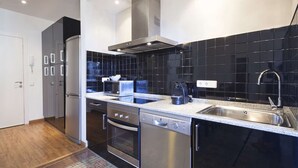 A modern kitchen with black tiled backsplash, stainless steel appliances, and a wooden floor. - Bright modernist apartment in Rambla Catalunya (Barcelona)