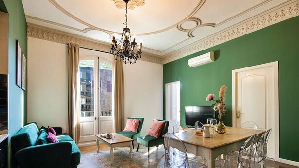 A living room with a green wall, a chandelier, a sofa, a coffee table, and a dining area with chairs. - Bright modernist apartment in Rambla Catalunya (Barcelona)