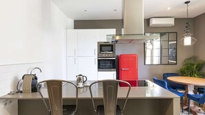 Una cocina moderna con armarios blancos, un refrigerador rojo y un comedor con sillas azules.