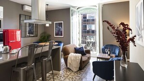 Una cocina moderna con un refrigerador rojo, una zona de comedor con un sofá azul y un ventanal con vistas a edificios.