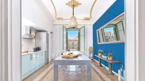 A narrow hallway with a dining table set for two, a kitchen on the left, and a blue wall with a mirror on the right. - Luxury and design in Rambla Catalunya (Barcelona)