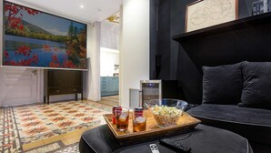 A living room with a large TV, a sofa, a coffee table with snacks, and a painting on the wall. - Luxury and design in Rambla Catalunya (Barcelona)