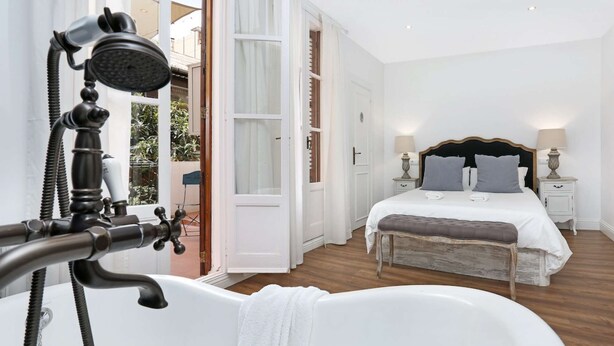 A bedroom with a large bathtub, a bed with two pillows, and a nightstand with a lamp.