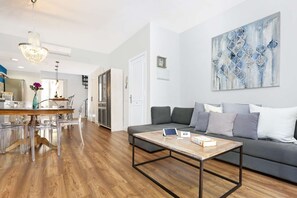 A modern living room with a wooden coffee table, grey sofa, and abstract art on the wall.