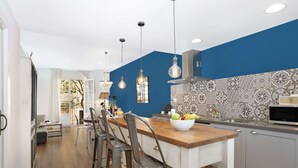 A modern kitchen with a blue accent wall, pendant lighting, and a fruit bowl on the counter.