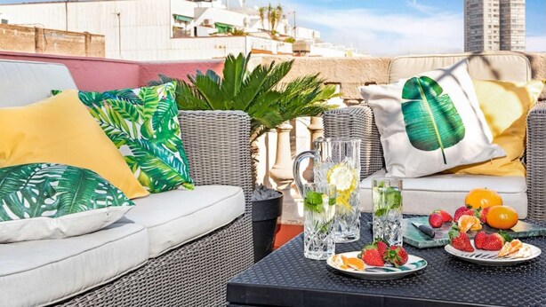 Una terrazza sul tetto con divano, mobili in vimini, un tavolo con frutta e bevande e vista sulla città.