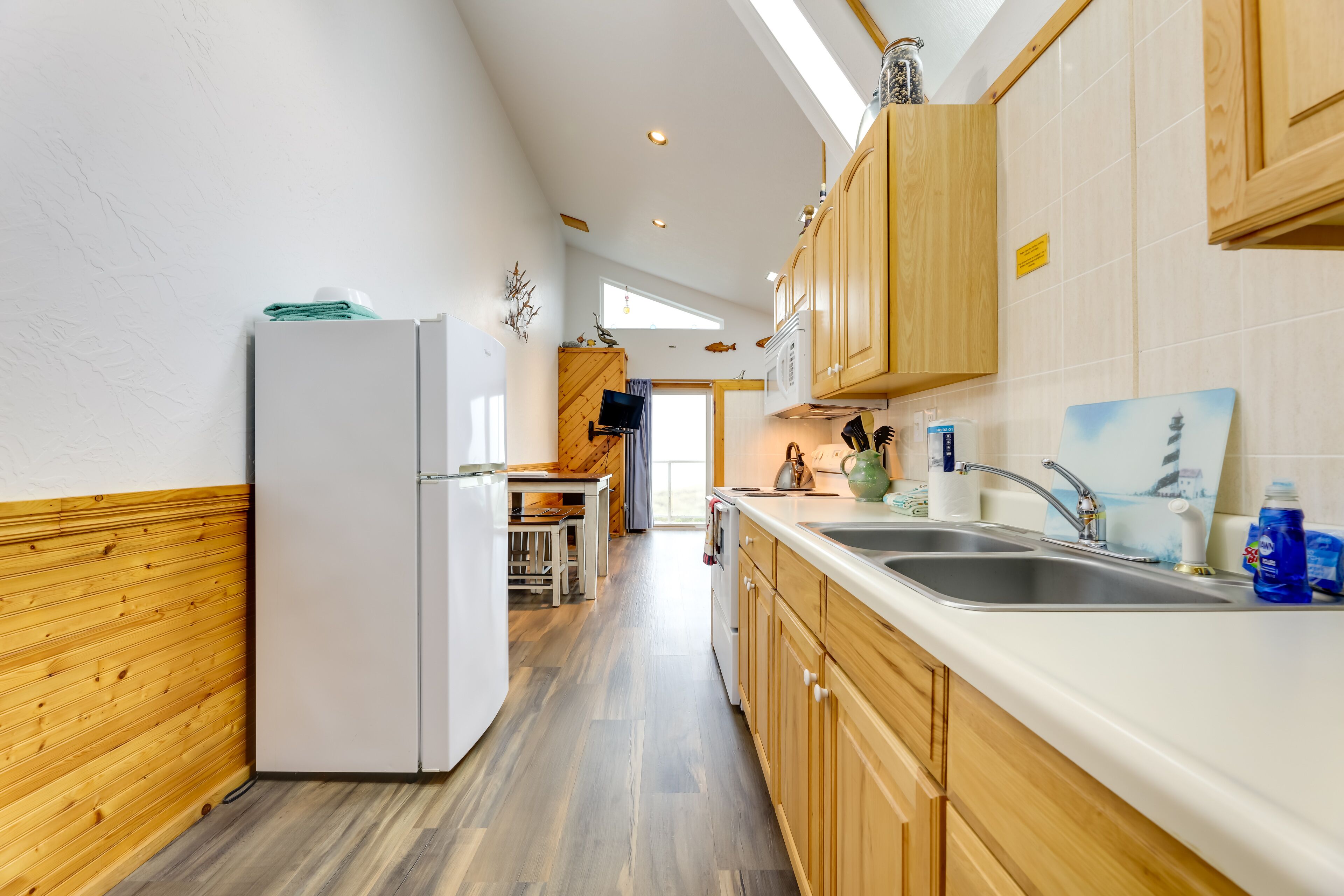 A modern kitchen with wooden cabinets, a white refrigerator, and a large window providing natural light.