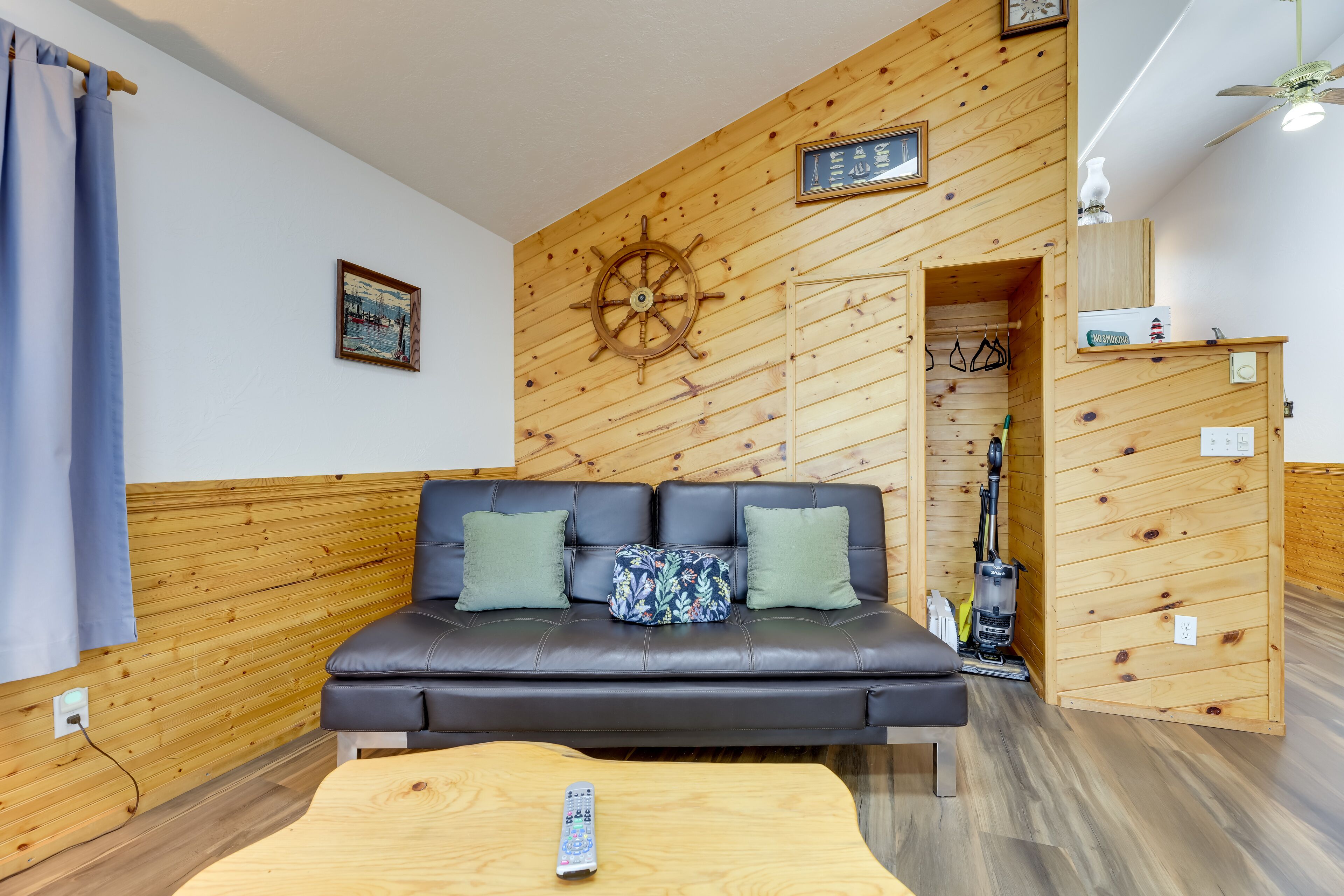 A room with a wooden wall, a black leather sofa with green cushions, a wooden coffee table, and a ceiling fan.