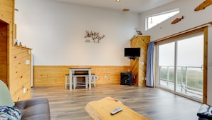 A spacious living area with a wooden floor, a fireplace, a television, and a balcony with a view.